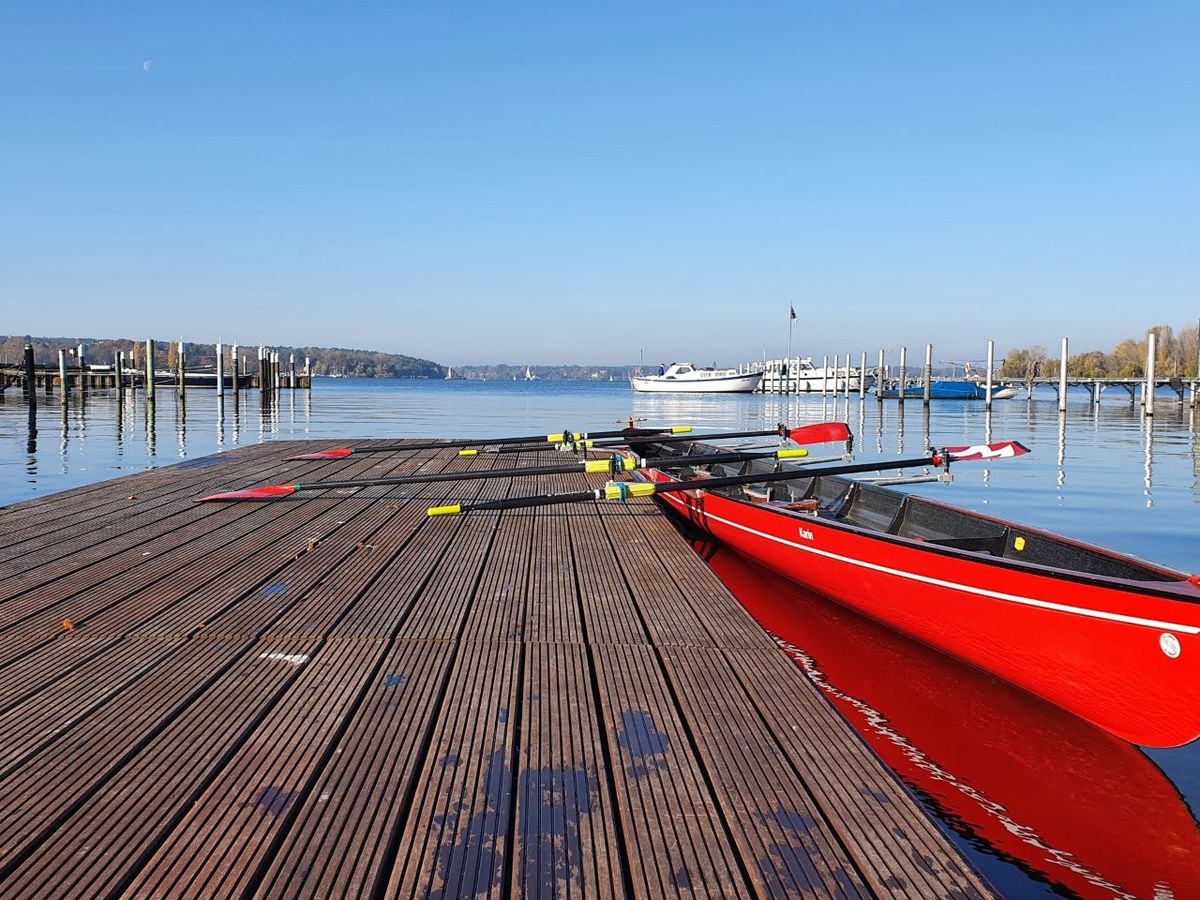 Ein Riemen-Vierer mit Steuermann liegt am Steg, im Hintergrund sieht man den grossen Wannsee.