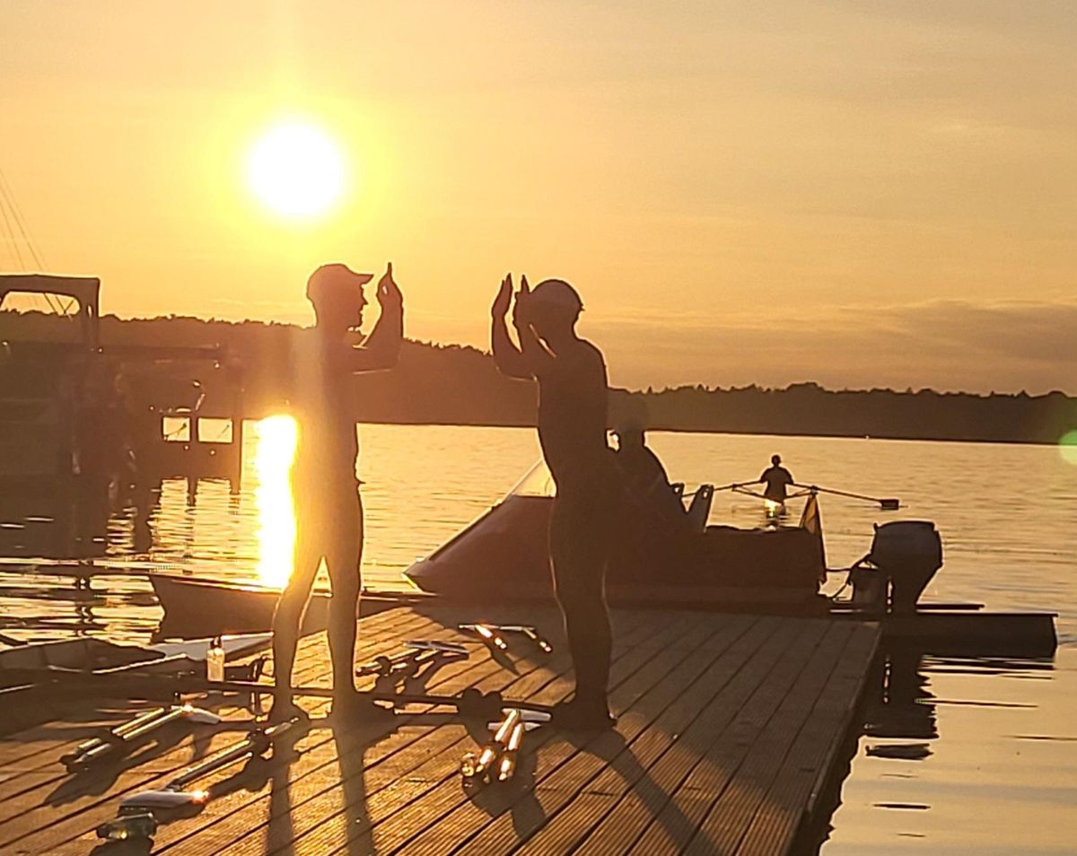 Zwei Ruderer klatschen sich im Sonnenuntergang auf dem Steg ab.